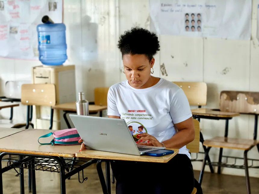 A woman in a classroom setting diligently working on a laptop while seated at a desk.