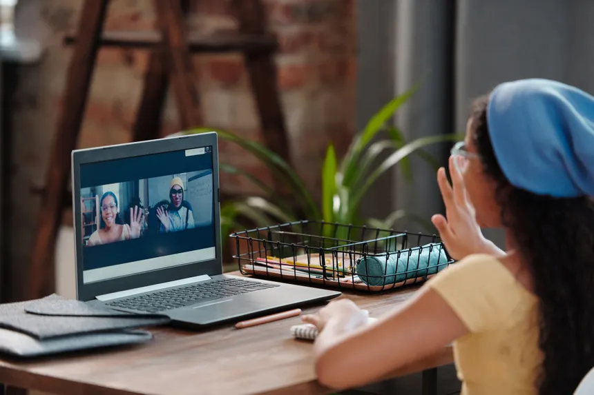 Young girl engaging in an online class from home, using a laptop and waving to her screen.