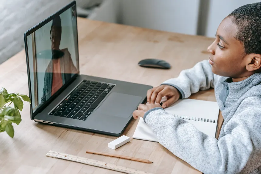 From above side view of crop African American schoolchild watching netbook with speaking female teacher during distance learning at table
