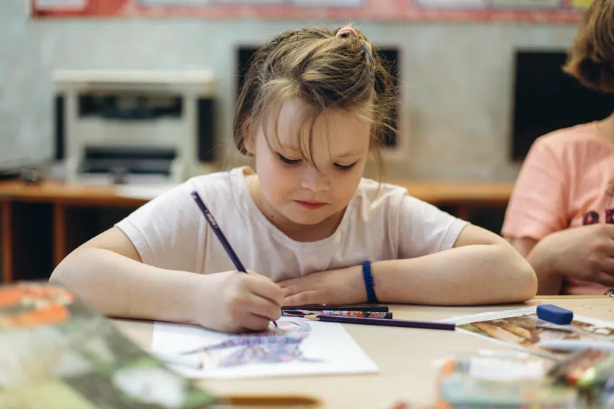 A child intensely focuses on coloring with pencils at a school desk, highlighting creativity and learning.