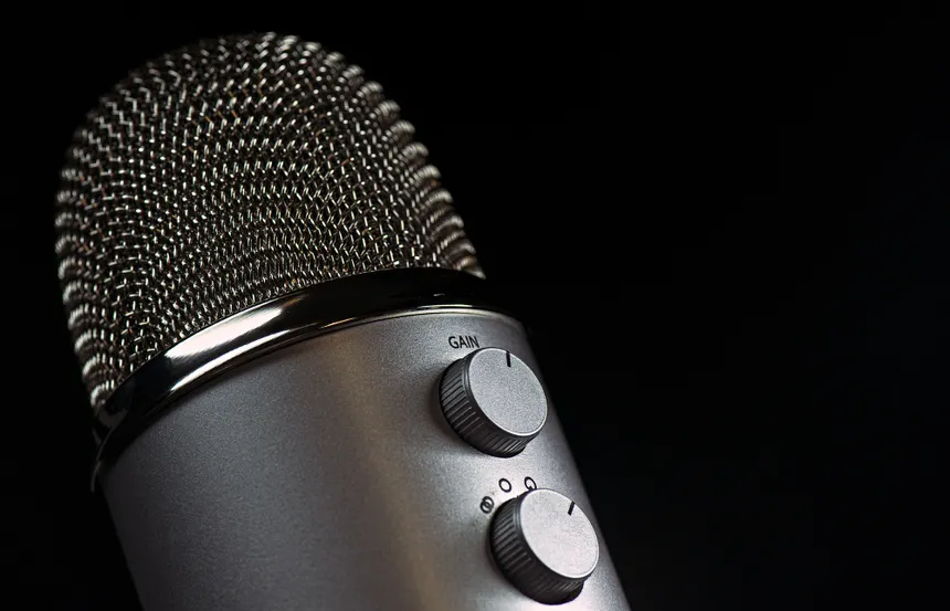 Detailed close-up of a silver mesh microphone with gain control knobs against a dark background.