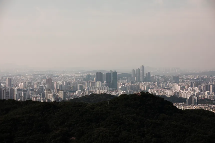 Aerial view of a vast city skyline with foreground hills, showcasing urban density.