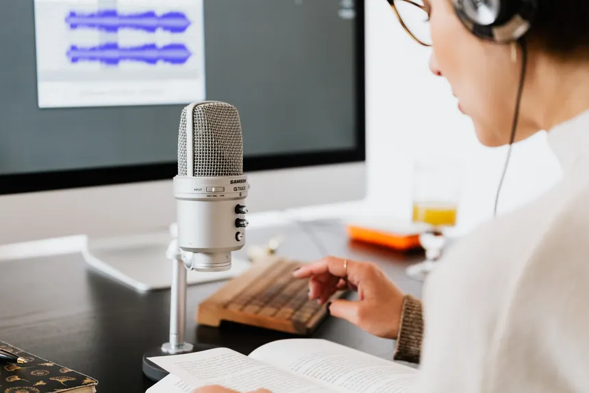 Person wearing headphones reading from a book with a microphone. Ideal for podcasts.