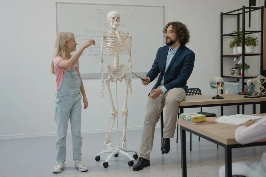 Teacher and student interact with a skeleton model during a lively biology lesson in a classroom.